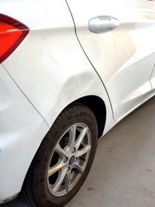 a white car with a large dent in the body work over the rear offside wheel